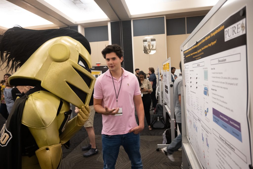 Researcher explains his research poster to Knightro, UCF's mascot.