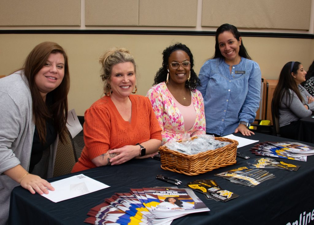 Four smiling women sitting behind a table advertising graduate programs at Grad Fair