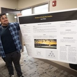 Graduate student Luis Rios holding up a poster in the GSC