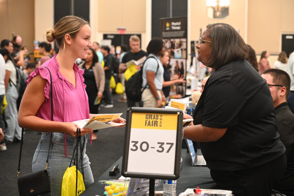 Two women smiling and speaking over a table at the 2025 UCF Grad Fair event.