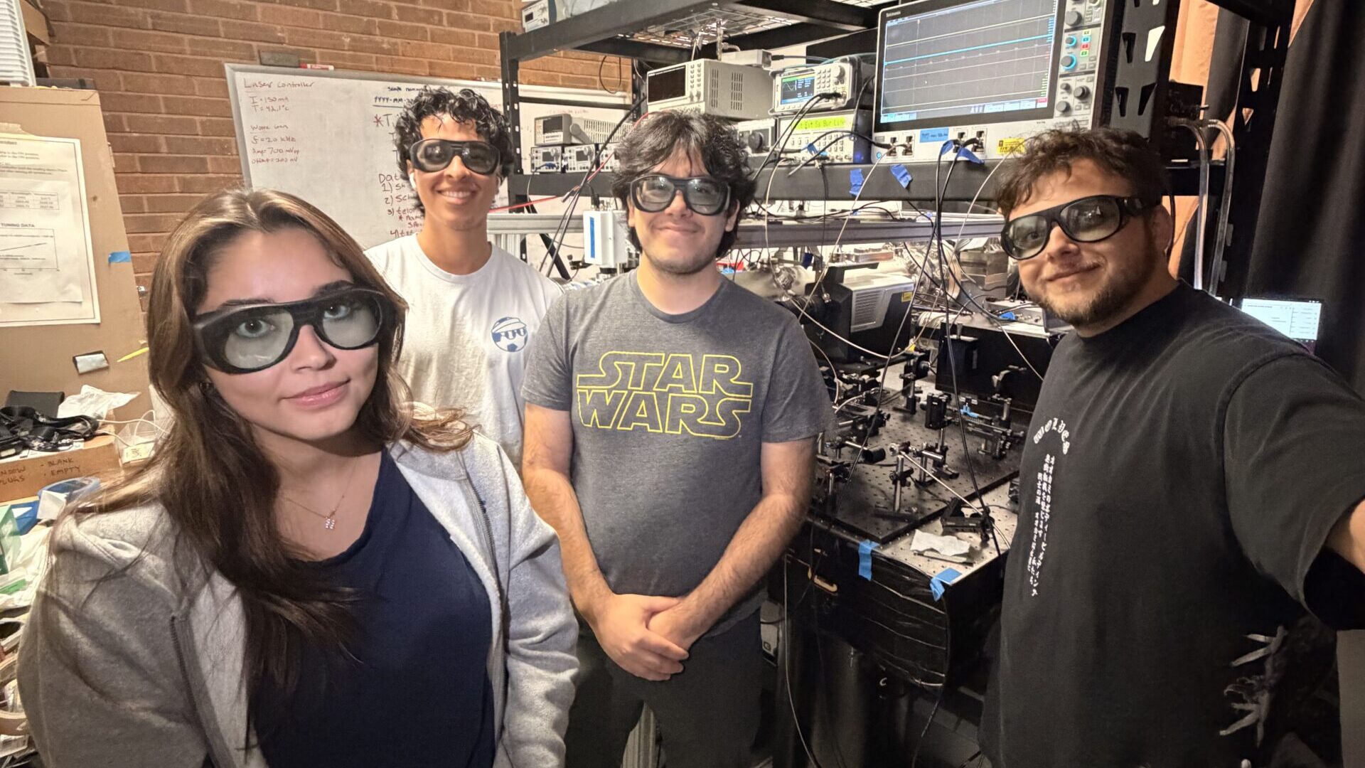 Four students with goggles standing in a lab